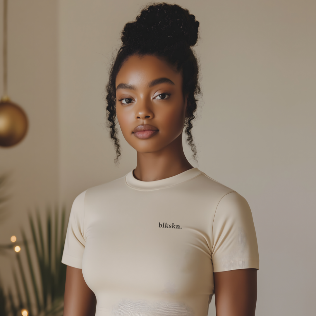 Woman wearing a beige t-shirt with 'blkskin.' text in a blurred indoor setting