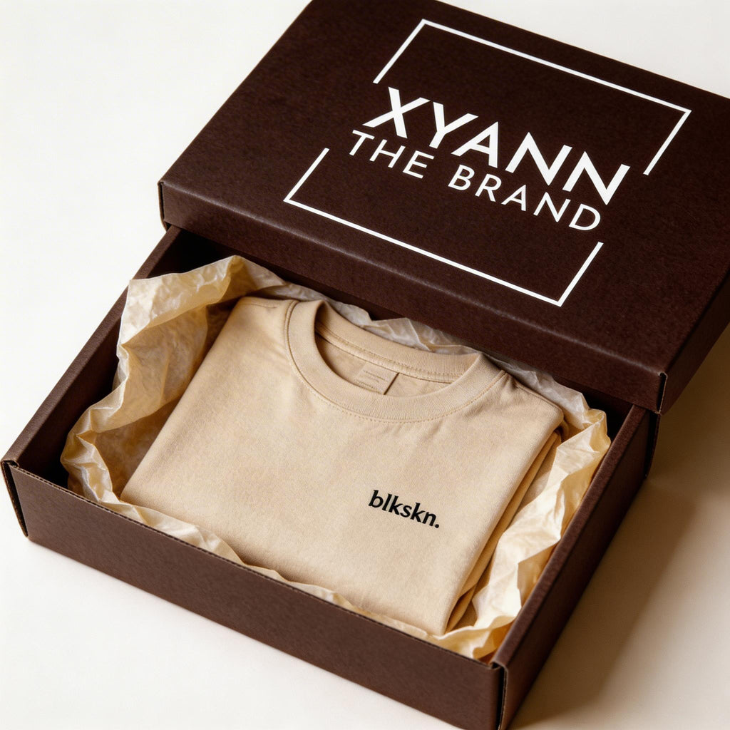 Beige t-shirt with 'blkskn.' logo in an open brown box labeled 'XYANN THE BRAND'.