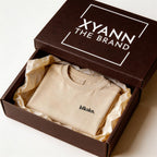 Beige t-shirt with 'blkskn.' logo in an open brown box labeled 'XYANN THE BRAND'.